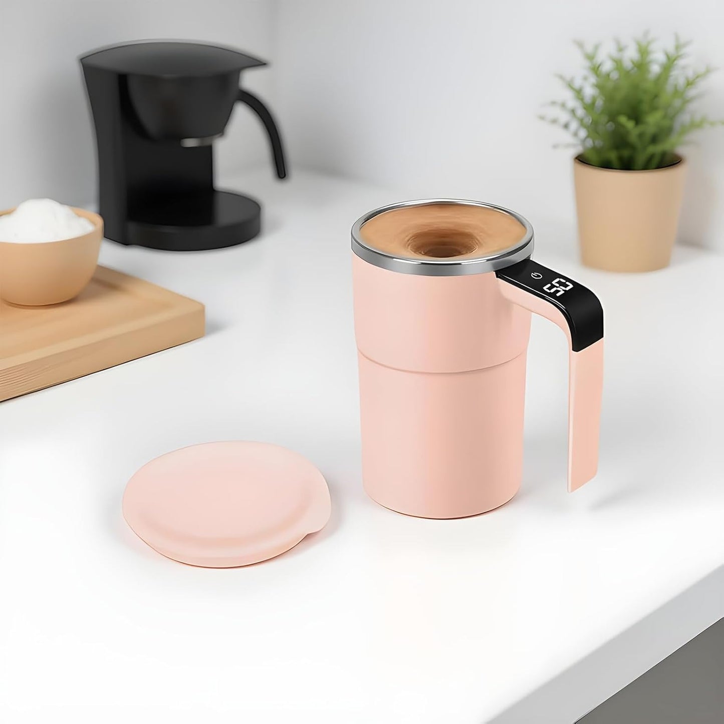 Pink coffee maker with wooden top on a white surface with a plant and coffee beans in the background